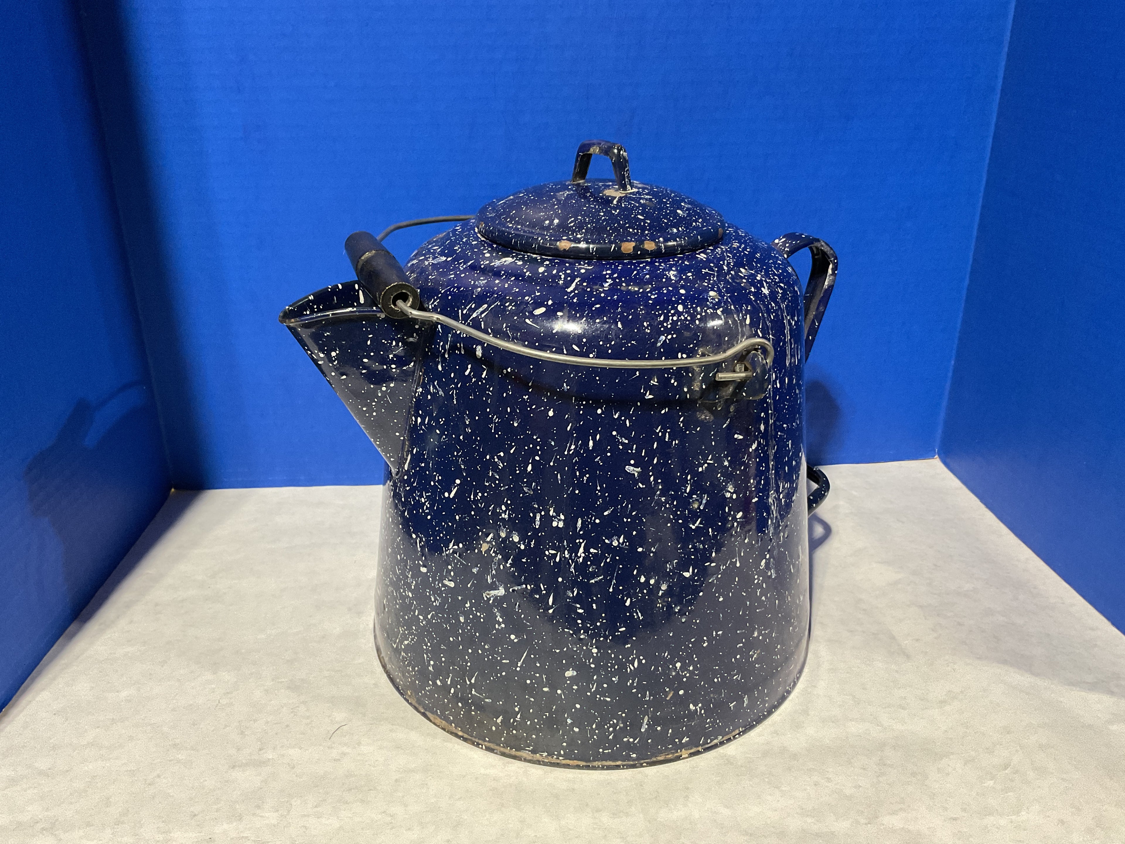 Blue speckled enamel teapot on a white surface with a blue background